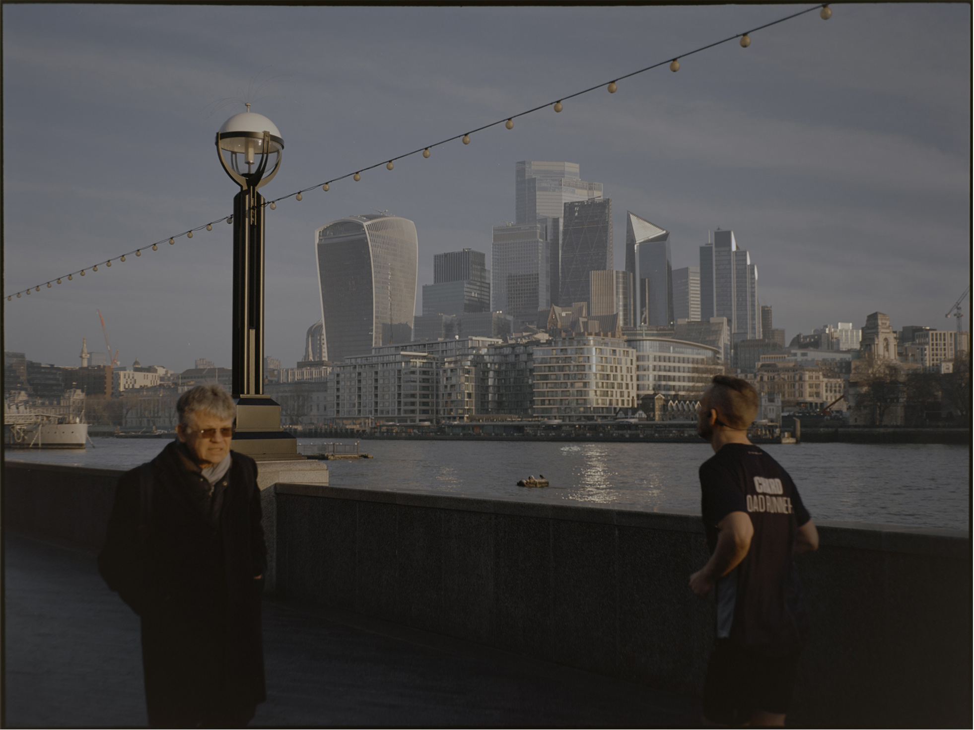 Two figures on the south bank with the City of London skyline and Thames — lifestyle street photography London