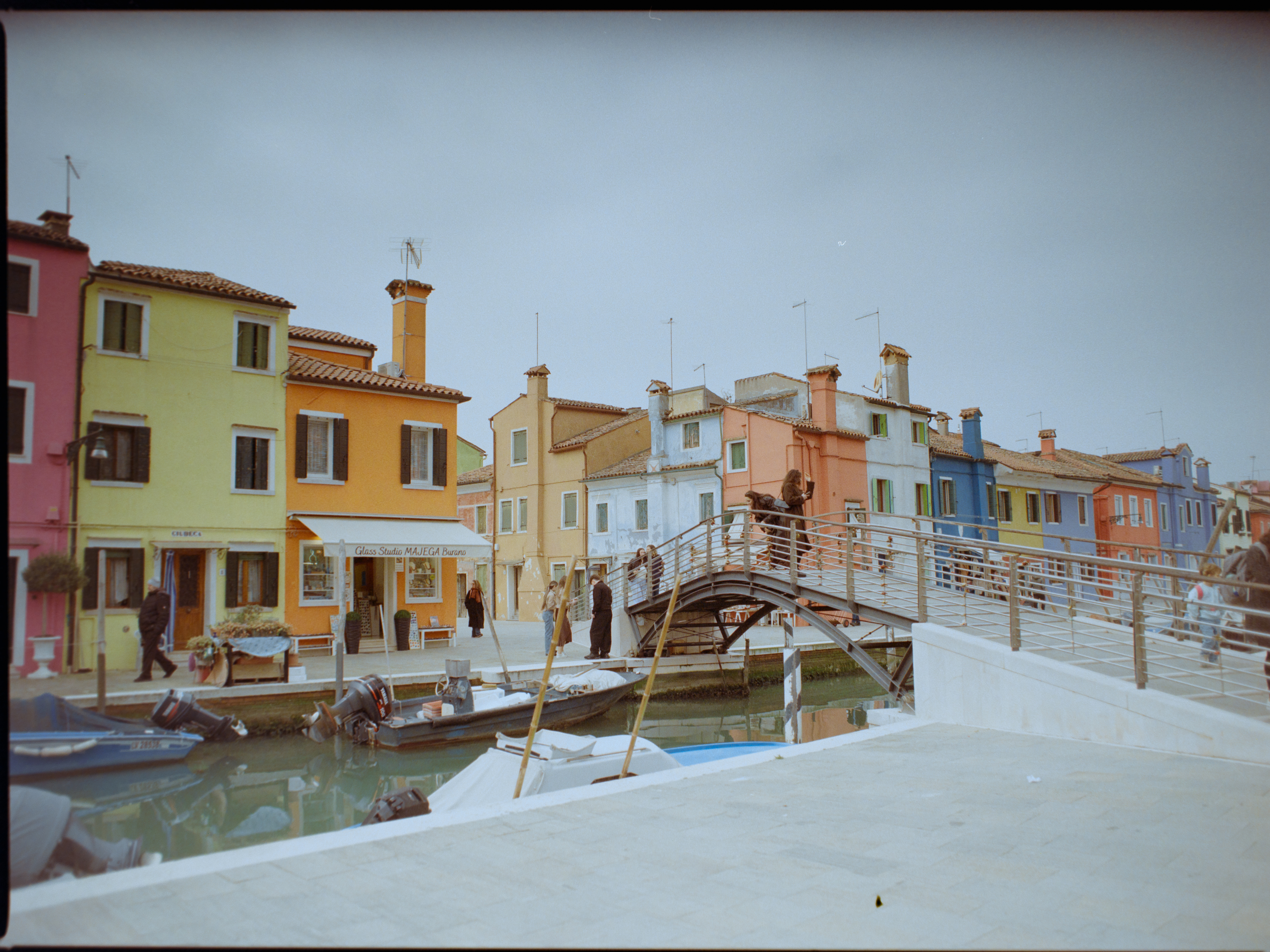 Wider canal view with pedestrian bridge and line of pastel houses on Burano — Venice on Kodak Gold 200