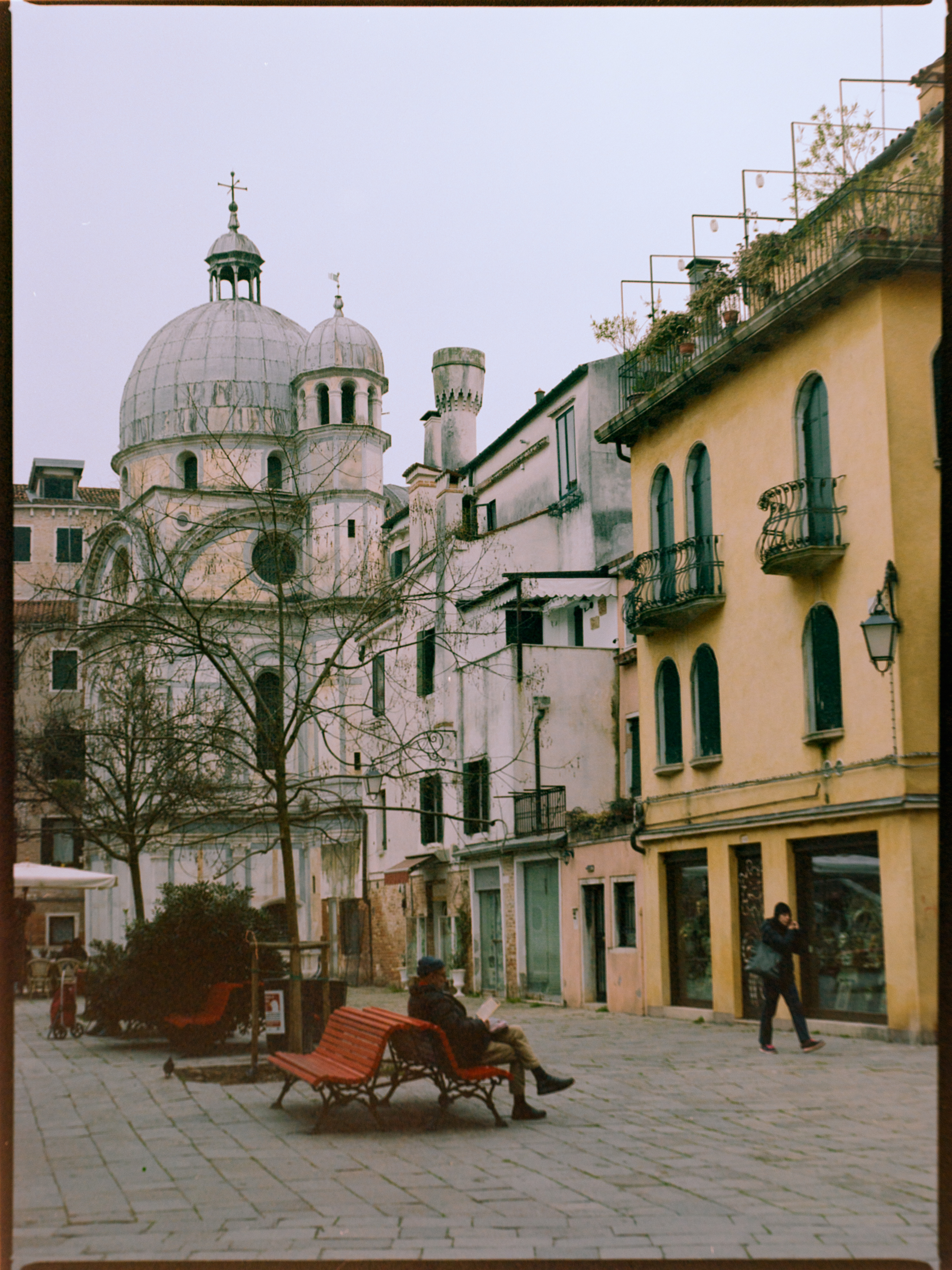 Quiet piazza with domed church and lone figure on a red bench — Venice on Kodak Gold 200