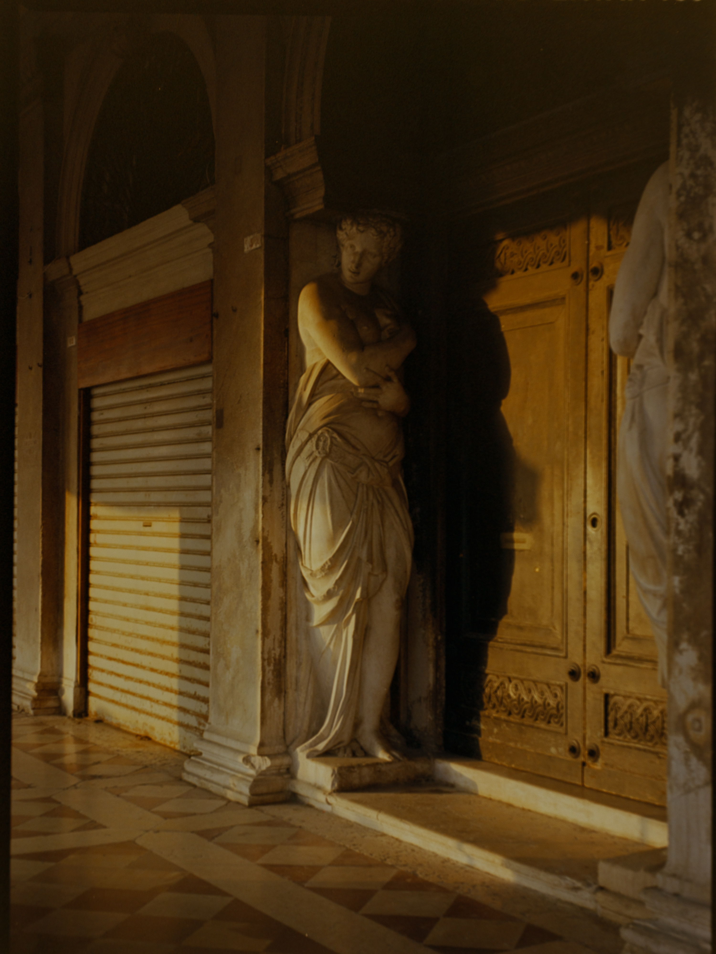 Classical marble statue lit by golden side-light inside the Procuratie arcade — Venice on medium format film